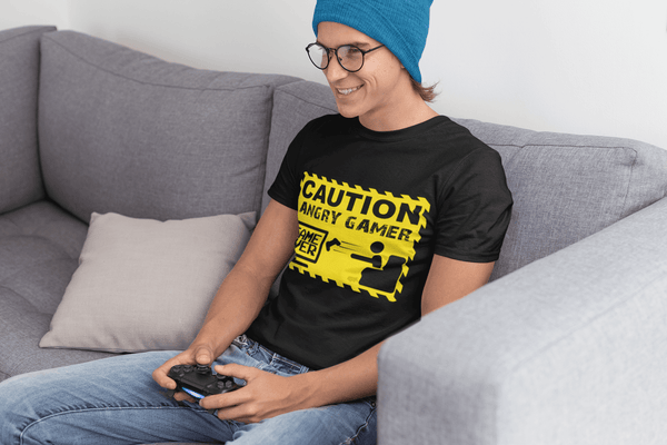 Guy sitting on couch playing video games wearing a black T-shirt with Caution Angry Gamer on the Front, now available from the Xpert Apparel Store  