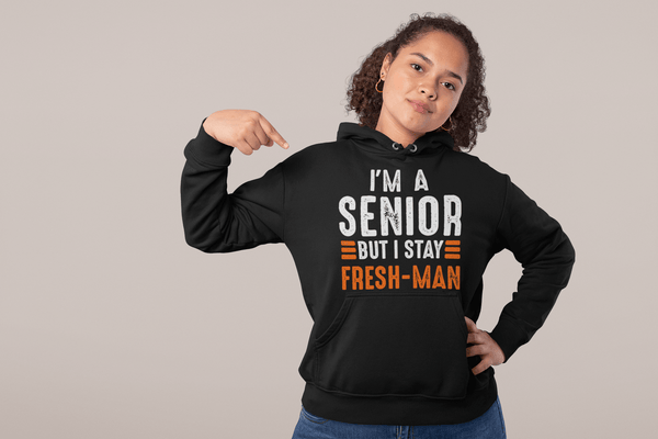 Girl  wearing black Hoodie pointing at the  I'm a Senior But I Stay Fresh-man T-shirt design from the Xpert Apparel Store
