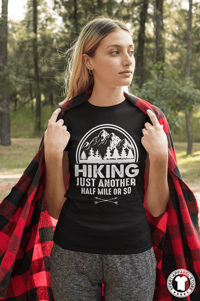 Young Woman Standing in the Park with a red and black "flannel blanket" and wearing a black t-shirt with "Hiking, just another half mile or so" design on the front. available from the Xpert Apparel Store.