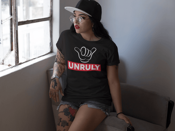 Sexy Hispanic girl sitting on arm of a chair with tattoo's on leg, wearing short jeans and a black T-shirt with Unruly design with cartoon fingers on the front, available from the Xpert Apparel Store.